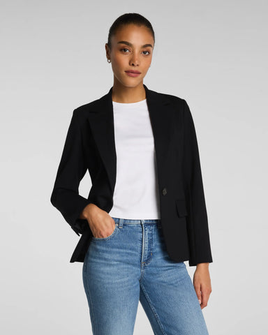 Person wearing a black blazer, white shirt, and blue jeans on a plain background