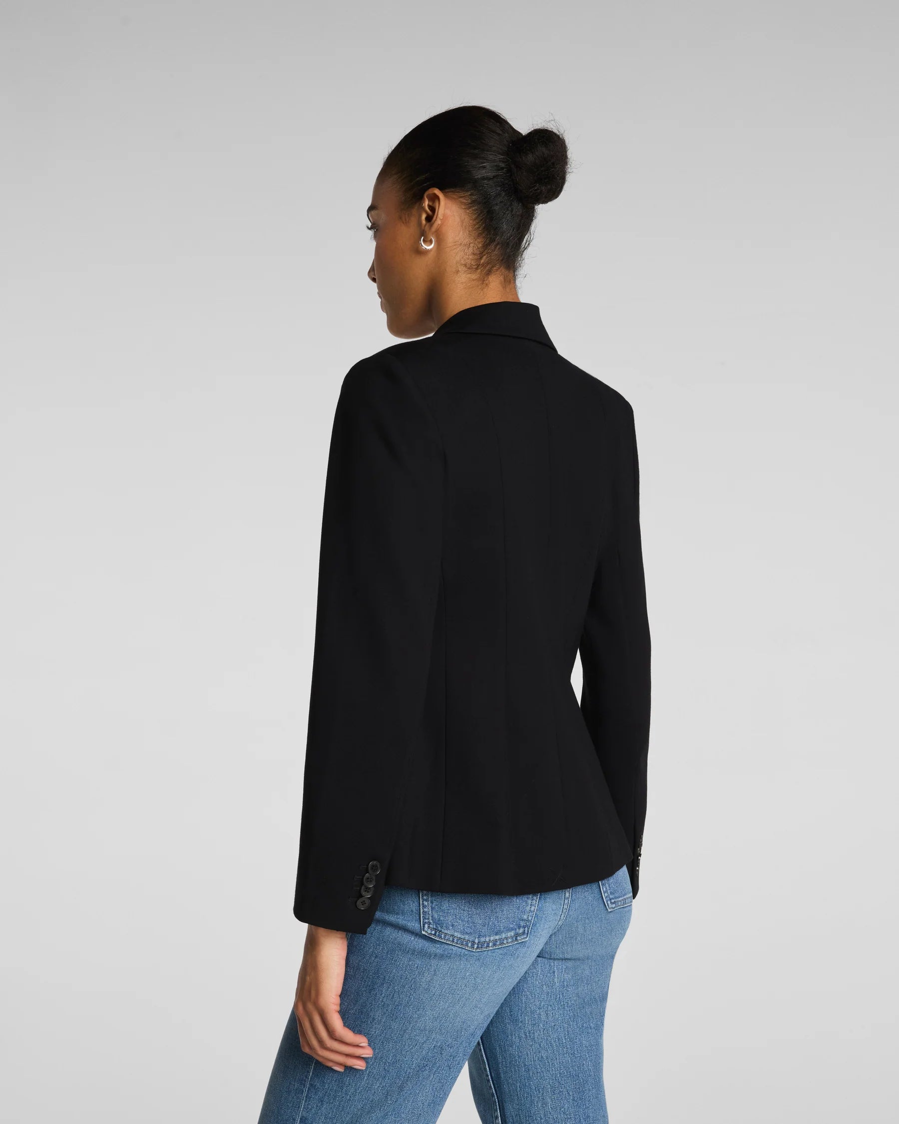 Person wearing a black blazer and blue jeans on a light gray background