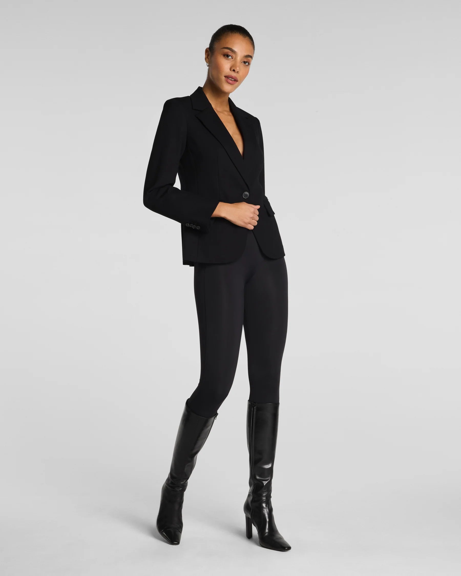 Woman wearing a black suit with black boots on a light gray background