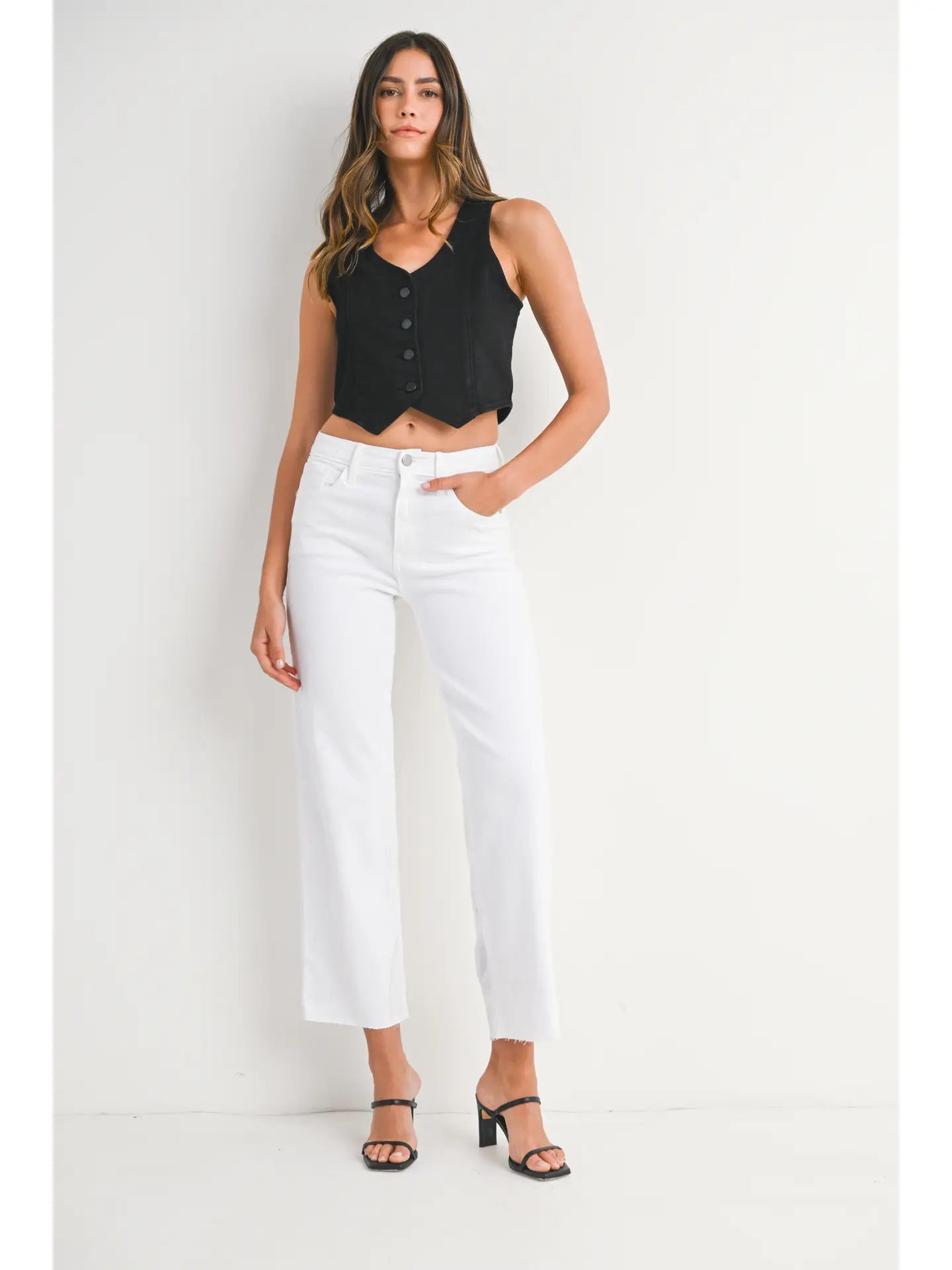 Woman wearing a black sleeveless top and white pants on a white background