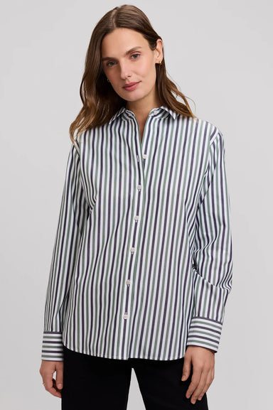 A woman wearing a long-sleeve button-up shirt with vertical navy and white stripes, paired with black pants, photographed against a solid light gray background.