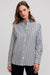 A woman wearing a long-sleeve button-up shirt with vertical navy and white stripes, paired with black pants, photographed against a solid light gray background.
