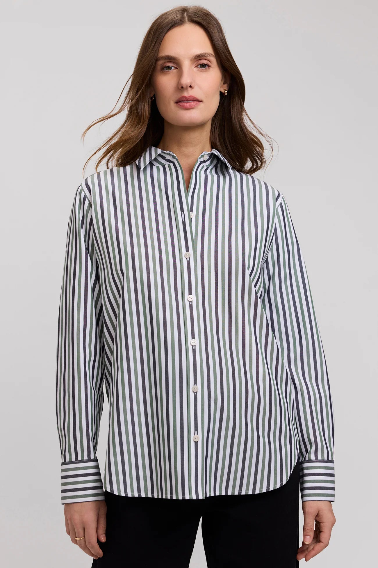 A woman wearing a long-sleeve button-up shirt with vertical navy and white stripes, paired with black pants, photographed against a neutral light gray studio background.