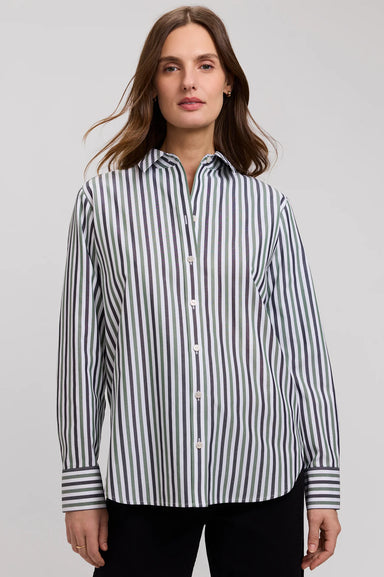 A woman wearing a long-sleeve button-up shirt with vertical navy and white stripes, paired with black pants, photographed against a neutral light gray studio background.