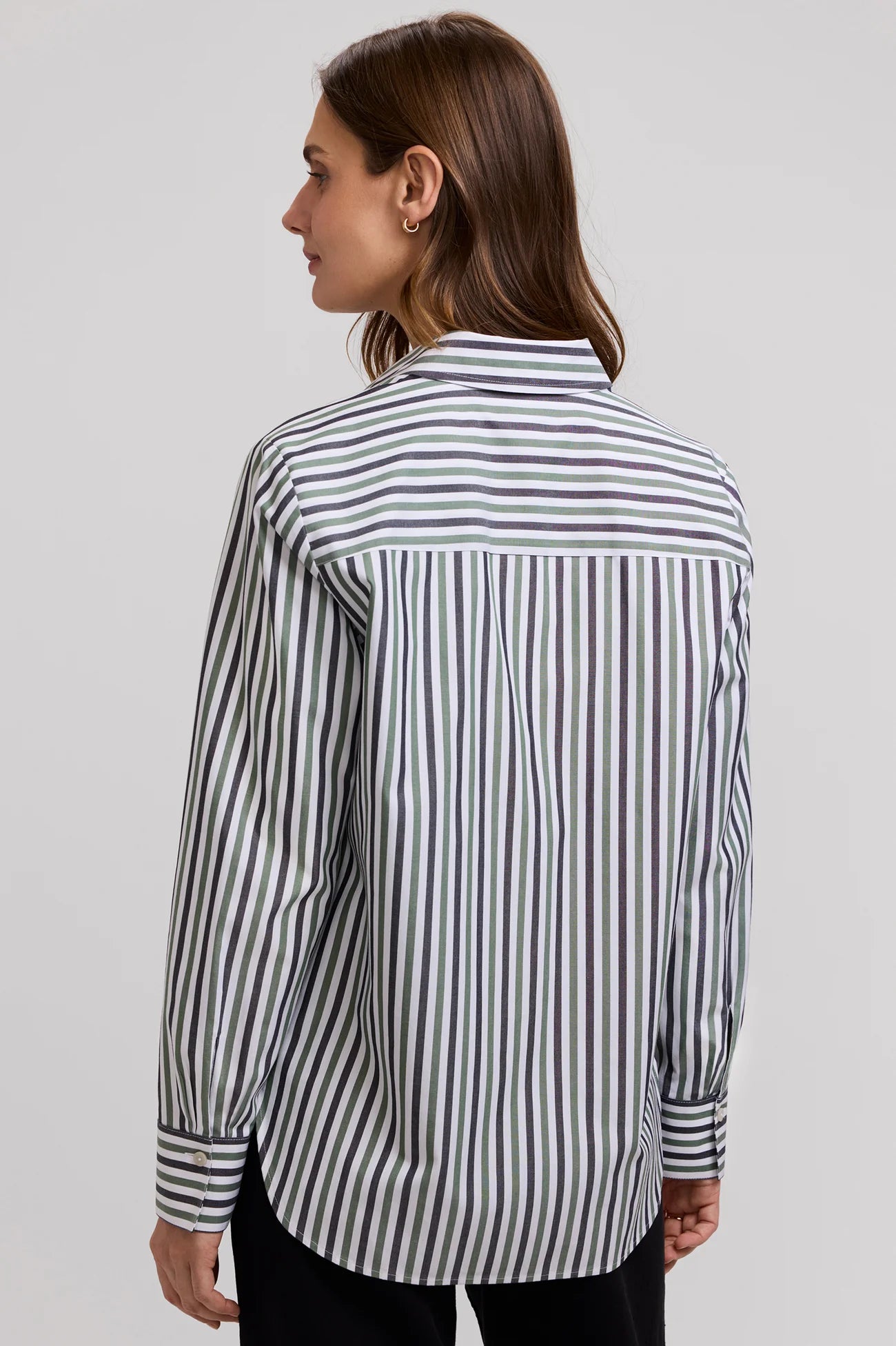 A woman shown from the back wearing a long-sleeve button-up shirt with vertical black and white stripes, paired with black pants, against a light gray studio background.