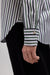 Close-up of a person wearing a striped button-up shirt with green, white, and black vertical stripes, paired with black trousers. The shirt sleeve is rolled up to show the cuff with a single button.