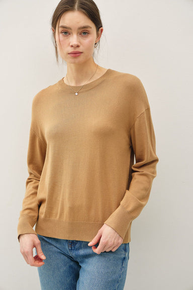 Woman wearing a brown sweater and blue jeans against a white background