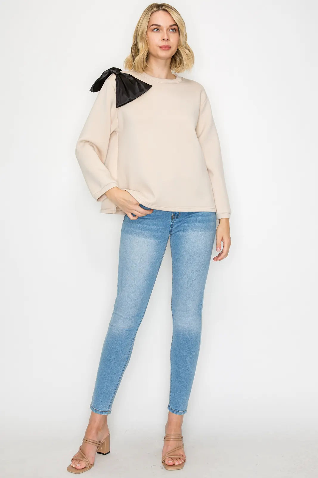 Woman wearing a beige sweater with black accents and blue jeans on a white background