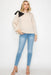 Woman wearing a beige sweater with black accents and blue jeans on a white background