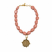 Necklace with pink beads and a gold coin pendant on a white background