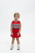 A young child stands against a plain white studio background wearing a red sleeveless dress with a horizontal stripe pattern across the chest featuring the word 'GEORGIA' in white with a red outline.