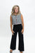 A woman modeling a sleeveless black and white gingham top with red and gold trim, paired with black wide-leg pants and black sandals, against a plain white studio background.