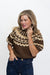 A woman modeling a brown knit sweater with a cream geometric pattern, paired with dark blue jeans, against a plain white background.
