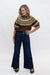 A woman modeling a brown short-sleeve knit top with a beige geometric pattern around the yoke, paired with dark blue wide-leg jeans and brown shoes, against a plain white studio background.