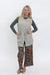 A woman modeling a light gray sleeveless button-front vest over a dark green long-sleeve top and brown wide-leg pants with a red and blue floral pattern, standing against a plain white studio background.