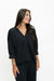 A woman wearing a black button-front cardigan top with three-quarter sleeves and black pants, photographed against a plain white studio background.