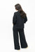 A woman with long dark hair is shown from the back wearing a black cropped long-sleeve top and matching wide-leg trousers, standing against a plain white studio background.