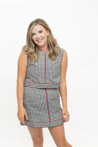 A woman modeling a sleeveless black and white gingham mini dress with red piping details, set against a plain white studio background.