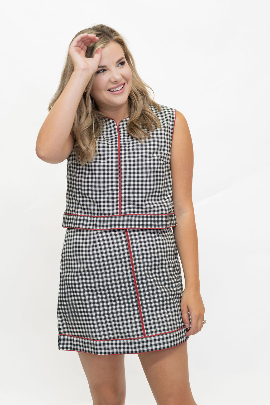 A woman modeling a sleeveless black and white gingham mini dress with red piping details, set against a plain white studio background.