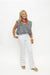 A woman modeling a sleeveless black and white striped top, white pants, a red beaded necklace, and gold bracelets against a plain white background.