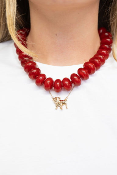 A close-up of a model wearing a chunky red beaded necklace with a small gold-tone dog pendant.