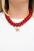 A close-up of a model wearing a chunky red beaded necklace with a small gold-tone dog pendant.