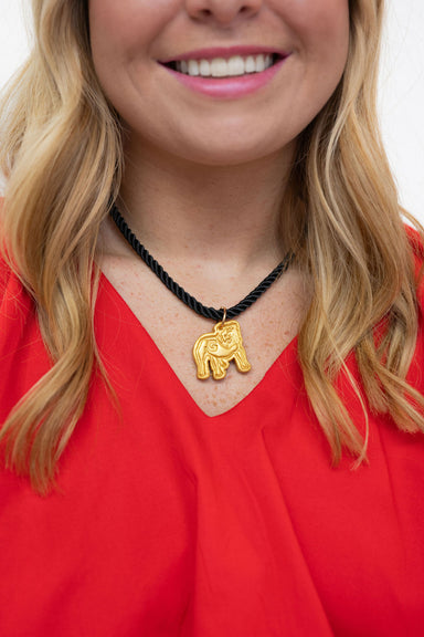 A close-up of a woman wearing a gold elephant pendant necklace on a black braided cord, paired with a bright red top.