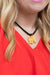 A close-up of a woman wearing a black braided cord necklace with a small gold elephant pendant, paired with a bright red top.