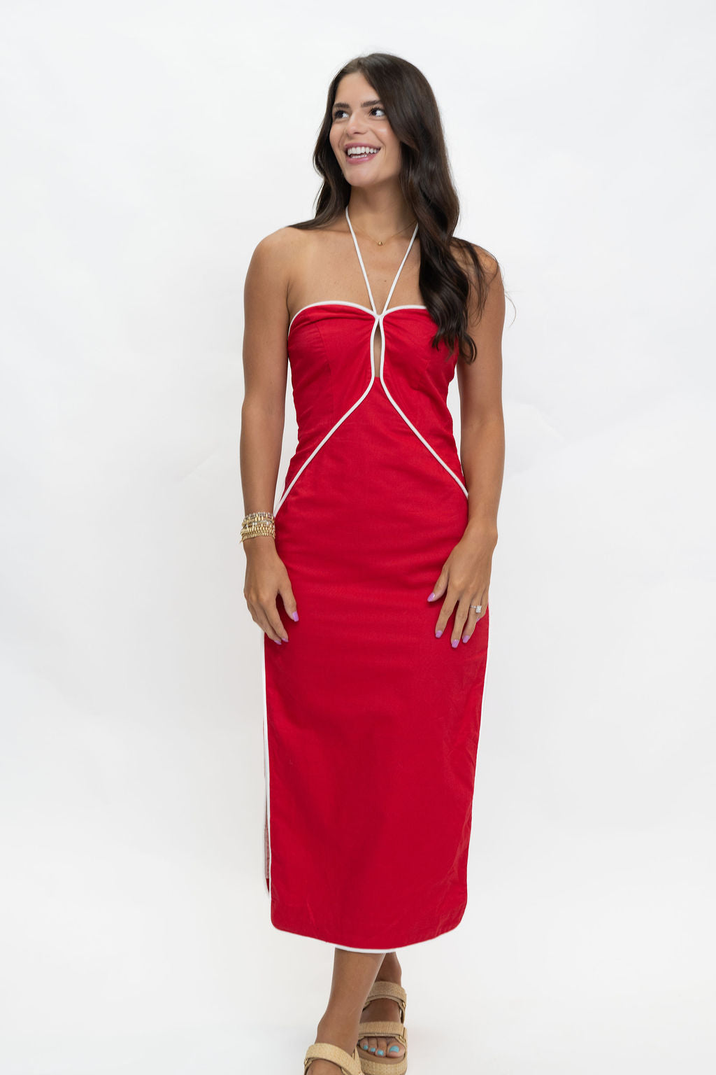 A woman modeling a bright red strapless halter maxi dress with white contrast piping details, standing against a plain white studio background.