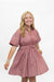 A smiling blonde woman wearing a short-sleeve pink and white vertically striped button-up dress with a gathered waist, standing against a plain white background.