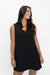 A woman modeling a sleeveless black shift dress with a notched lapel collar, paired with a red and yellow statement necklace, against a plain white studio background.