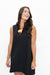 A woman wearing a sleeveless black shift dress with a split neckline and a gold elephant pendant necklace, posing against a solid white background.