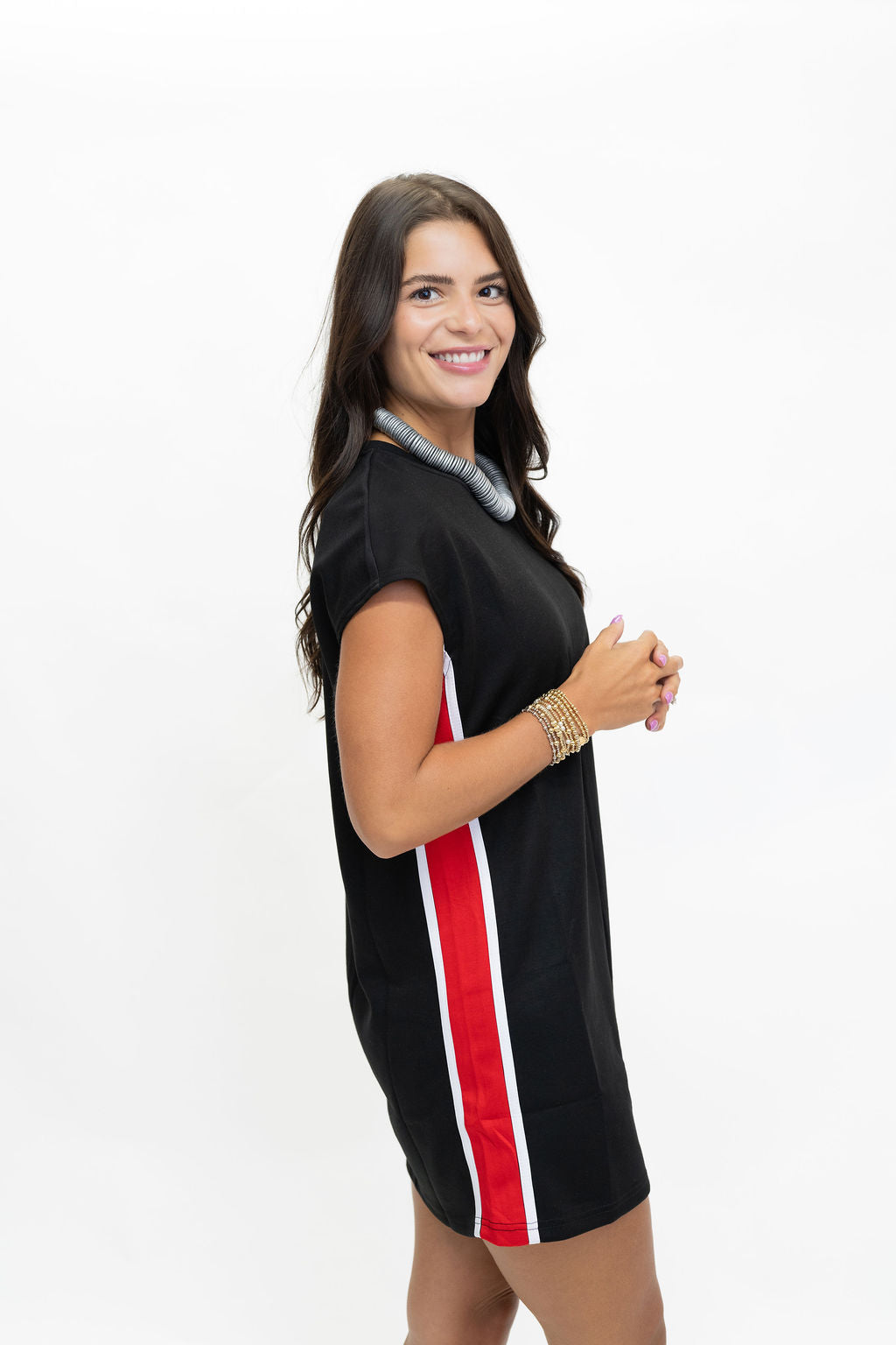 A woman modeling a black short-sleeve mini dress with a vertical red and white stripe down the side, posed against a plain white background.