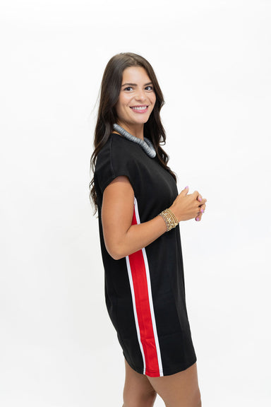 A woman modeling a black short-sleeve mini dress with a vertical red and white stripe down the side, posed against a plain white background.