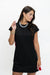 A woman modeling a black short-sleeve shift dress with a textured gray statement necklace and gold bracelets, posed against a plain white studio background.