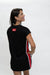 A woman wearing a black short-sleeve mini dress with red and white side stripes and a red square logo patch on the back, photographed against a plain white studio background.