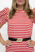 A close-up of a woman wearing a red and white horizontally striped short-sleeve top with a black belt featuring a gold football-shaped buckle, set against a plain white background.
