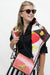 A woman wearing tortoiseshell sunglasses, a black top, and a colorful fruit-patterned scarf, carrying a red and white checkered handbag with a gold clasp against a plain white background.