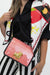 A close-up of a person wearing a red-and-white gingham crossbody bag with a gold bull emblem and a black-and-white striped top, while also wearing a white scarf with fruit and chain graphics.