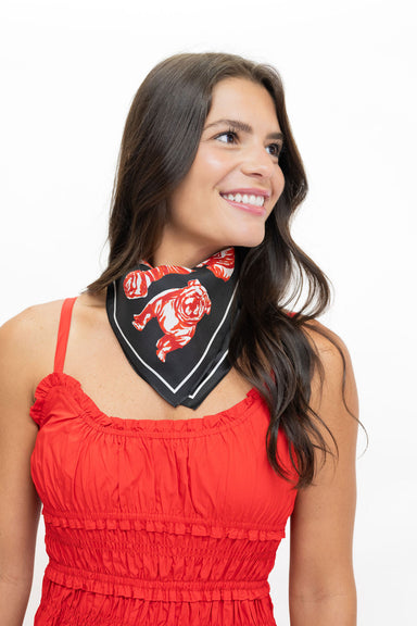 A woman with long dark hair wearing a red sleeveless top and a black neck bandana with a red bulldog graphic, photographed against a plain white background.