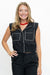 A smiling blonde woman wearing a black sleeveless vest with white contrast stitching and matching black pants, posed against a plain white studio background.