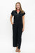 A woman modeling a black short-sleeve jumpsuit with a half-zip collar and wide-leg cropped pants, standing against a plain white studio background.