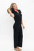 A woman modeling a black wide-leg jumpsuit with a split neckline and short sleeves, paired with a red beaded necklace and flat sandals, against a plain white studio background.