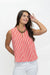 A woman wearing a sleeveless red and white vertically striped top with a high collar, paired with white pants and a chunky gold necklace, posing against a plain white background.