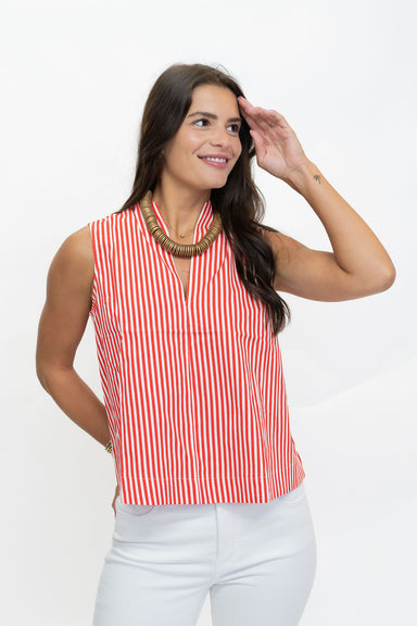 A woman wearing a sleeveless red and white vertically striped top with a split V-neckline, paired with white pants, posing against a plain white studio background.