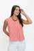 A woman wearing a sleeveless red and white vertically striped top with a split V-neckline, paired with white pants, posing against a plain white studio background.