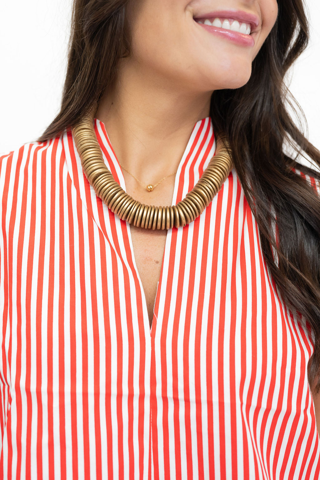 A close-up of a woman wearing a chunky, wide-brimmed gold statement necklace over a red and white vertically striped top.