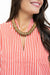 A close-up of a woman wearing a chunky, wide-brimmed gold statement necklace over a red and white vertically striped top.