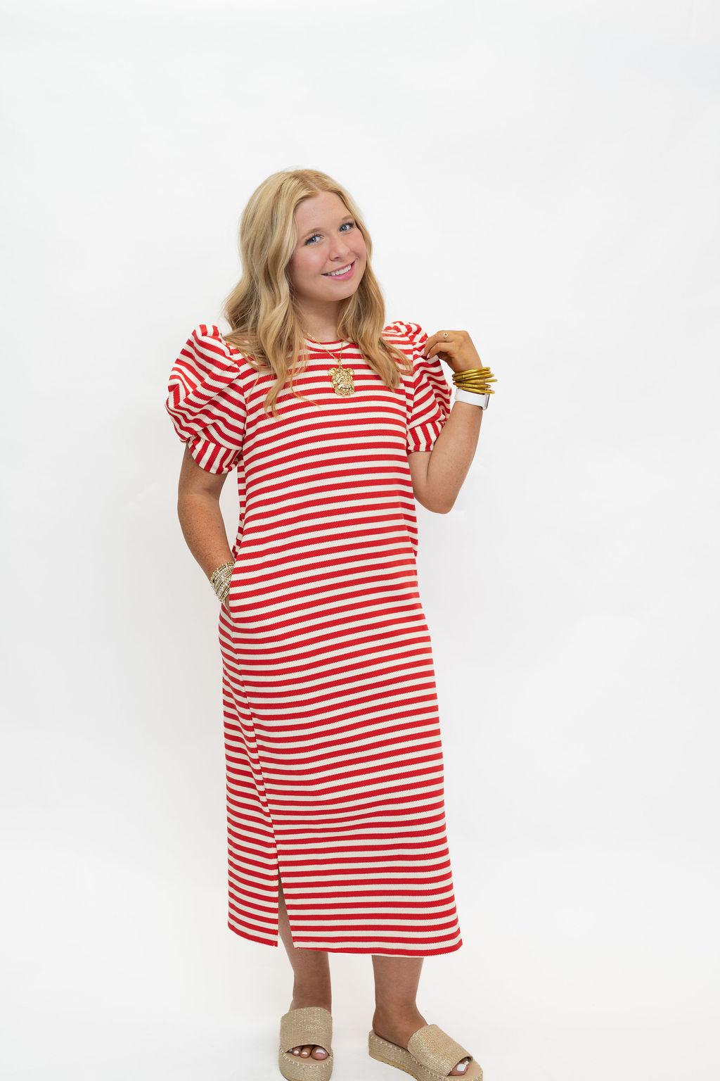 A woman modeling a red and white horizontally striped midi dress with puff sleeves, standing against a plain white studio background.