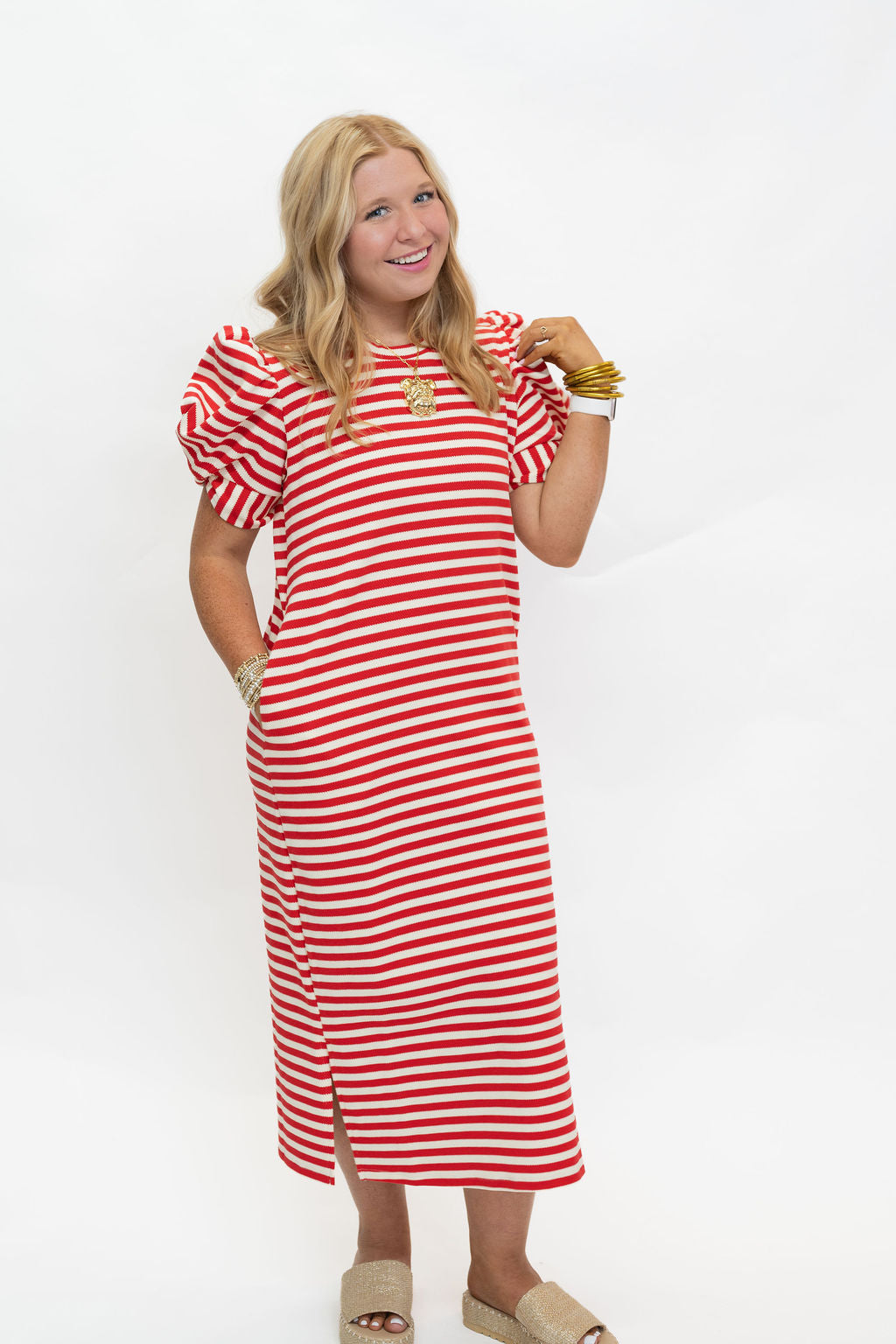A woman modeling a red and white horizontally striped midi dress with puff sleeves, standing against a plain white studio background.